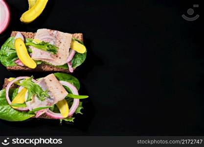 Open sandwich with young herring is a traditional Danish smorrebrod. Sandwiches with matias herring are located on a dark background with copy space. top view