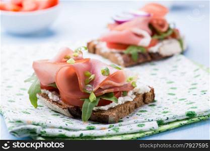 Open sandwiches with ham, tomato and arugula on green napkin, selective focus