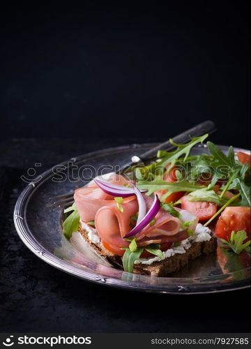 Open sandwiches with ham, tomato and arugula on metal vintage plate. Fresh salad on side, selective focus