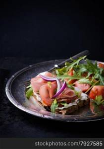 Open sandwiches with ham, tomato and arugula on metal vintage plate. Fresh salad on side, selective focus
