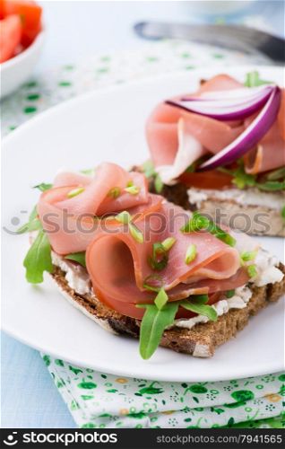 Open sandwiches with ham, tomato and arugula on plate, selective focus