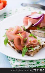 Open sandwiches with ham, tomato and arugula on plate, selective focus