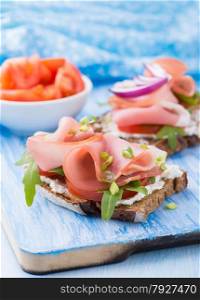 Open sandwiches with ham, tomato and arugula over blue background, selective focus