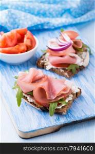 Open sandwiches with ham, tomato and arugula over blue background, selective focus
