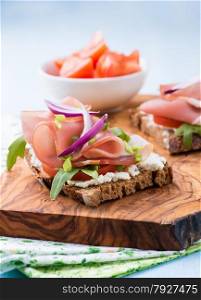 Open sandwiches with ham, tomato and arugula over olive wood board, low angle, selective focus
