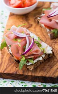 Open sandwiches with ham, tomato and arugula over olive wood board, top view, selective focus