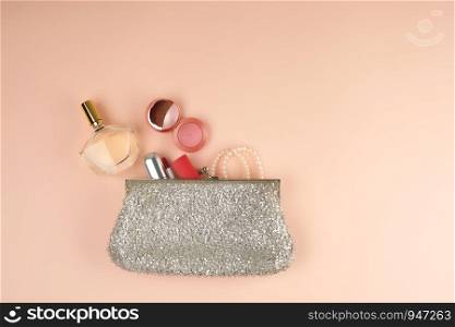 open silver clutch and cosmetics fell out of the middle, peach background, top view, copy space