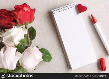 Open spiral notebook with stripes and a wooden clip with red heart pinned on it and a bouquet of white and red roses, on a vintage fabric background.