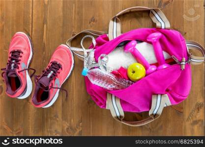 open sports bag and pink running shoes on a wooden floor top view
