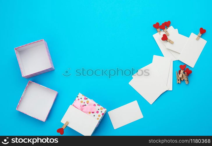 open square cardboard empty box and white blank paper rectangular business cards on decorative clothespins, item lies on a blue background, top view, copy space