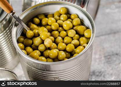 Open tin can with canned green peas with a spoon. On a gray background. High quality photo. Open tin can with canned green peas with a spoon.
