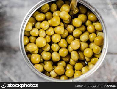 Open tin can with canned green peas with a spoon. On a gray background. High quality photo. Open tin can with canned green peas with a spoon.