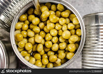 Open tin can with canned green peas with a spoon. On a gray background. High quality photo. Open tin can with canned green peas with a spoon.