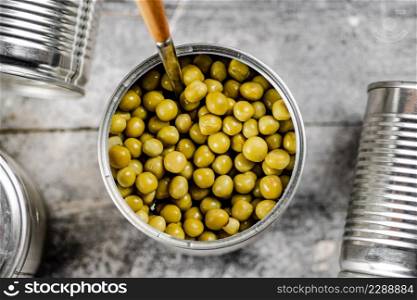 Open tin can with canned green peas with a spoon. On a gray background. High quality photo. Open tin can with canned green peas with a spoon.