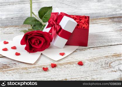 Open Valentines gift box filled with candies and single red rose on rustic white wood in close up view
