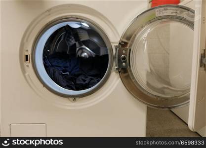 Open washing machine with some clothes inside drum