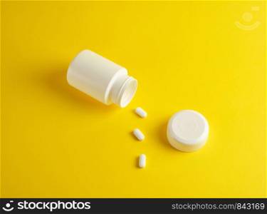 open white plastic jar for medicines and oval pills on a yellow background, blank for design and lettering