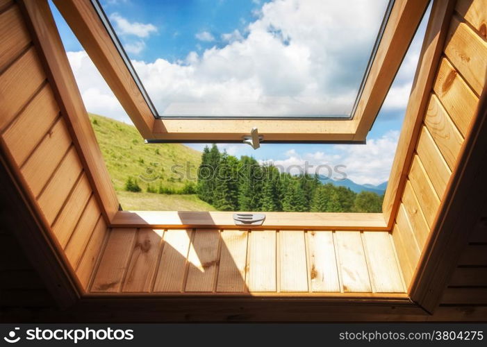 Open window at village wooden house in mountains. Amazing view of summer landscape with forest and meadow under blue sky