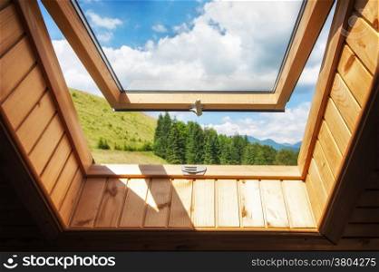 Open window at village wooden house in mountains. Amazing view of summer landscape with forest and meadow under blue sky