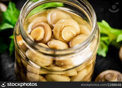 Opened a glass jar of pickled mushrooms. On a black background. High quality photo. Opened a glass jar of pickled mushrooms.