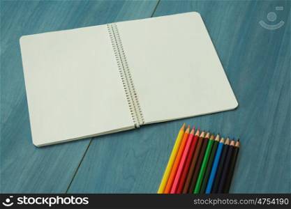 Opened blank notebook and color pencils on a wooden blue background