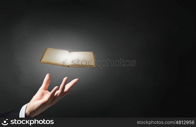Opened book in hand. Hand of man holding old book on dark background