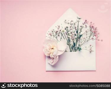 Opened envelop with flowers arrangement on pastel pink background, top view, copy space. Creative greeting, Invitation and holiday concept