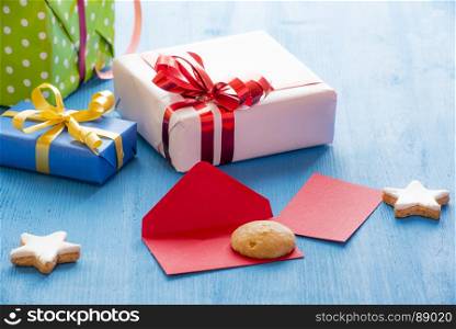 Opened envelope on a blue wooden table, surrounded by gingerbread stars shape cookies and gift boxes
