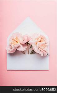 Opened envelope with Peonies flowers arrangements on pink background, top view. Festive greeting concept