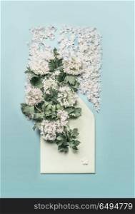 Opened envelope with white flowers and blossom arrangements on pastel blue background, top view. Festive greeting concept. Invitation or card for wedding, birthday and other holidays