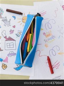 opened pencil case with wax crayons placed kid drawings