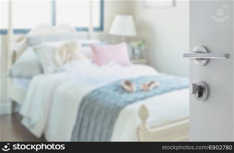 opened white door to bedroom with pillows and doll on white bed