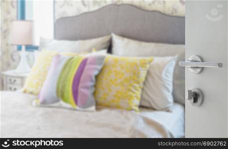 opened white door to blurred colorful pillows on bed in a modern house