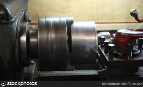 Operator turning part by manual lathe machine. Cutting tool processing steel metal shaft on lathe turning machine in workshop.
