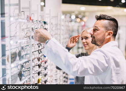 Optician and his patient choosing glasses. Proffesional medical advisor, correction eyewear.. Optician and his patient choosing glasses.