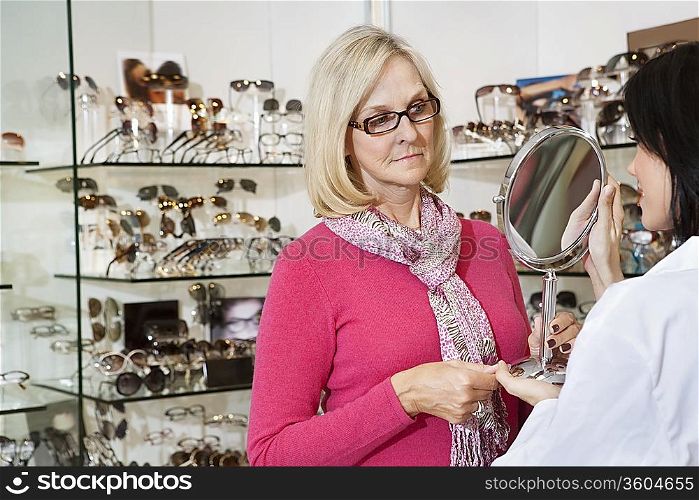 Optician holding mirror while senior female customer looking