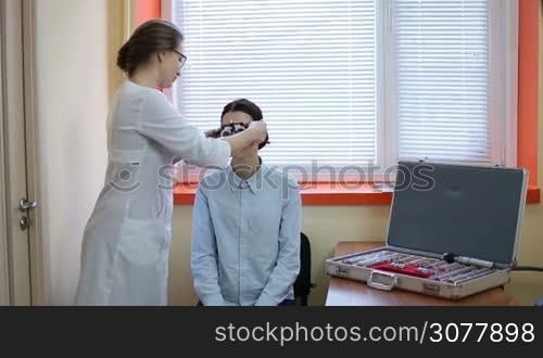 Optometrist examining female patient with trial frame in ophthalmology clinic. Female ophthalmologist with trial frame checking female patient vision at eye clinic. Professional eye doctor examining human vision in oculist office.