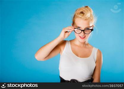 Optometrist, oculist and ophthalmologist concept. Young blonde retro pin up smiling woman with eyeglasses on blue background in studio.