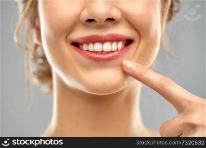 oral care, dental hygiene and people concept - close up of finger pointing to woman face with healthy white teeth over gray background. close up of woman pointing to her white teeth