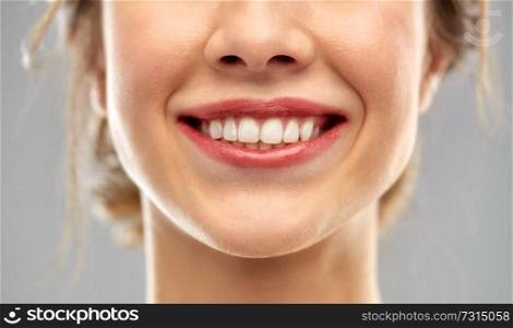 oral care, dental hygiene and people concept - close up of smiling woman face with white teeth over gray background. close up of smiling woman face with white teeth