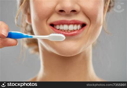 oral care, dental hygiene and people concept - close up of smiling woman with toothbrush cleaning teeth over gray background. close up of woman with toothbrush cleaning teeth