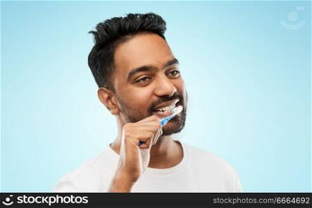 oral care, dental hygiene and people concept - smiling young indian man with toothbrush cleaning teeth over blue background. indian man with toothbrush cleaning teeth