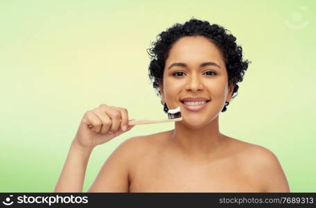 oral care, dental hygiene and sustainability concept - smiling african american woman with wooden toothbrush cleaning teeth over lime green natural background. smiling woman with toothbrush cleaning teeth