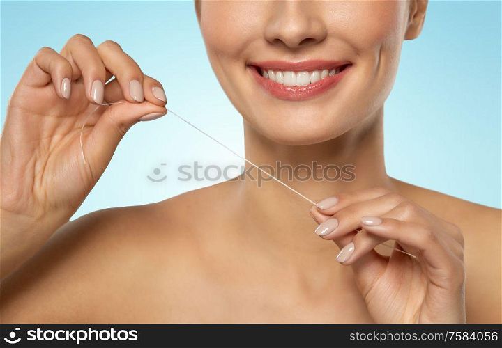 oral hygiene, dental care and health concept - close up of smiling young woman with floss cleaning teeth over blue background. smiling woman with dental floss cleaning teeth