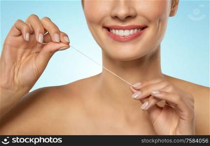 oral hygiene, dental care and health concept - close up of smiling young woman with floss cleaning teeth over blue background. smiling woman with dental floss cleaning teeth