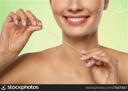 oral hygiene, dental care and health concept - close up of smiling young woman with floss cleaning teeth over lime green natural background. smiling woman with dental floss cleaning teeth