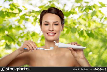 oral hygiene, dental care and health concept - smiling woman with toothbrush and toothpaste cleaning teeth over green natural background. smiling woman with toothbrush cleaning teeth