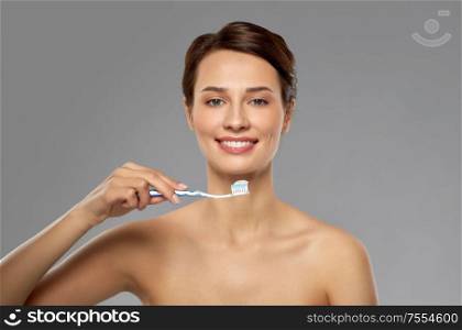 oral hygiene, dental care and health concept - smiling woman with toothpaste on toothbrush cleaning teeth over grey background. smiling woman with toothbrush cleaning teeth