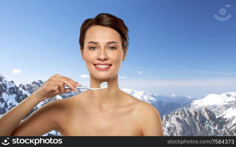 oral hygiene, dental care and health concept - smiling woman with toothpaste on toothbrush cleaning teeth over snowy alps mountains on background. smiling woman with toothbrush cleaning teeth