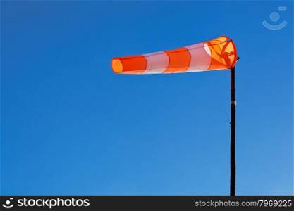 Orange and white windsock blows against a blue sky.